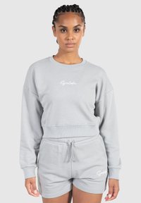 Grå cropped sweatshirt med ribbede manchetter og kant, der har et hvidt scripts logo. Matcher med grå shorts, der også har logo detaljer.