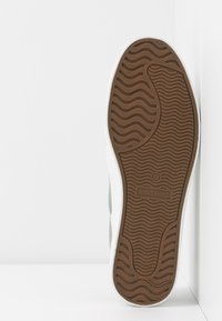 Semelle de chaussure blanche avec motifs de bande de roulement en caoutchouc marron et nom de la marque « ANNA FIELD » sur fond blanc.