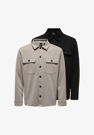 Zwei langärmlige Hemden mit Knöpfen und Kragen, vordere Klappentaschen; eines beige vorne, eines schwarz dahinter auf weißem Hintergrund.