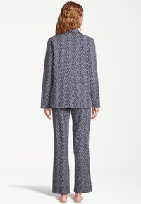 Marinblå pyjamasset som har en blazer-inspirerad överdel och matchande utsvängda byxor, prydda med små vita prickar på ett mjukt tyg.
