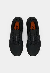 Schwarze Sportschuhe mit Obermaterial aus Netz und Synthetik, strukturierte Oberfläche, schwarze Schnürsenkel und orangene Einlegesohlen mit "TERREX"-Logo.