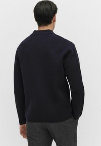 Marinblå stickad tröja med krage och långa ärmar. Tyget ser ut att vara texturerat och mjukt, med en avslappnad passform.