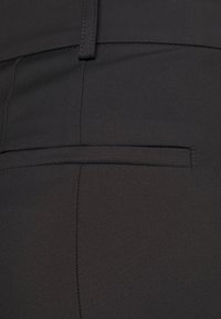 Svart tyg med en slät textur, med en bakficka som har en sydd söm och rena linjer, vilket betonar en skräddarsydd design.