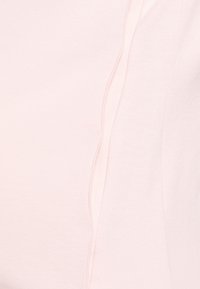 Top rosa claro feito de tecido macio com design sem emendas, apresentando uma textura subtil e um detalhe de costura minimalista ao longo do lado.