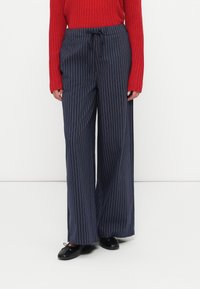 Pantalons larges rayés marins avec taille à cordon, associés à un pull côtelé rouge et des chaussures plates noires.