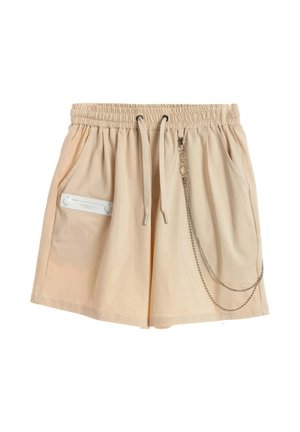 Pantalones cortos beige con cintura elástica y cordón, bolsillos laterales, detalle de etiqueta blanca en el bolsillo izquierdo y accesorio de cadena plateada adjunto en el lado derecho.