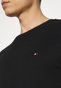 Camiseta de algodón negra con cuello redondo, mangas cortas y un pequeño logo bordado en rojo, blanco y azul en el pecho.