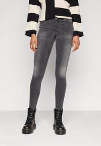 Grey skinny jeans with a faded finish, five-pocket design, and belt loops, paired with black lace-up boots and a black-and-white striped sweater.