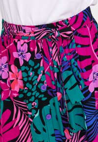 Spódnica w kwiaty z intensywnymi różowymi, zielonymi i purpurowymi wzorami na czarnym tle. Zawiera zawiązywany pasek w talii oraz purpurowe guziki.