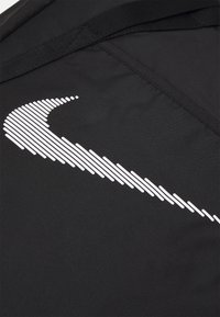 Close-up van zwarte stof met een gestileerd wit swoosh-logo gemaakt van horizontale lijnen, met details van de naad en band.