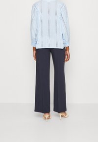 Blusa azzurra chiara con motivi verticali ad occhio di pernice, abbinata a pantaloni larghi scuri. Design semplice, vestibilità comoda e polsini arricciati.