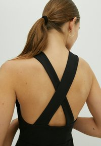 Schwarzes Kleid mit einem Kreuzrücken-Design, ärmelloser Schnitt und glatter Stofftextur. Minimalistischer Stil ohne zusätzliche Muster oder Verzierungen.