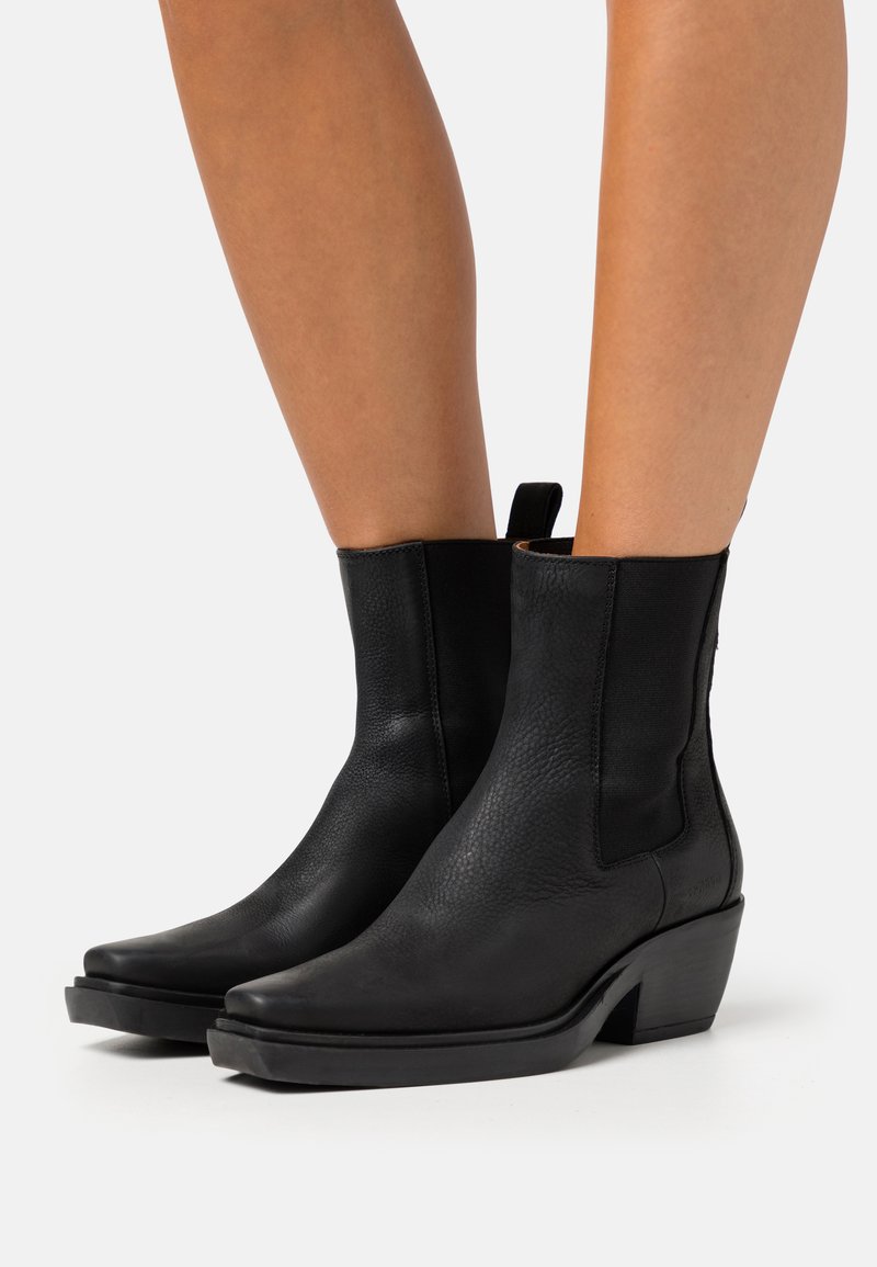 Botines negros de cuero texturizado, con punta afilada y un tacón bajo de bloque. Paneles elásticos laterales para facilitar su uso.