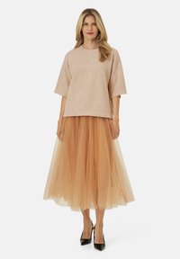 Beige tekstureret striktop med korte ærmer, parret med en lagdelt nude tylnederdel, suppleret af sorte spidse hæle.