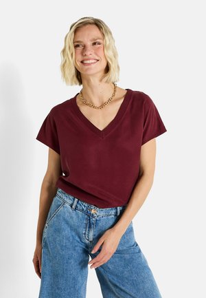 Camiseta corta de manga con escote en V color burdeos, fabricada en tejido suave, combinada con unos vaqueros de tiro alto en azul claro. Diseño sencillo y corte relajado.
