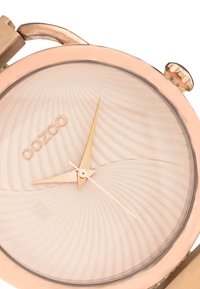 Montre en or rose avec un cadran texturé de couleur claire présentant des motifs ondulés et des aiguilles élégantes. Le nom de la marque "oozoo" est embossé sur le cadran.