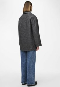 Cappotto di lana grigio con colletto ampio, vestibilità oversize e maniche lunghe. Abbinato a jeans in denim blu larghi e scarpe nere.