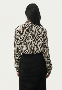 Bluse med lange ærmer i beige med sort zebra-print. Har en afslappet pasform og manchetærmer, parret med en struktureret sort nederdel.