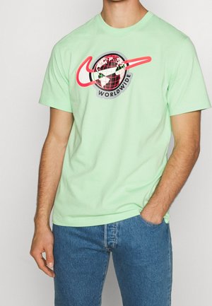 Miętowo-zielona bawełniana koszulka z okrągłą czarno-czerwoną grafiką globu, napisem "WORLDWIDE" oraz czerwonym logo Nike w kształcie haka.