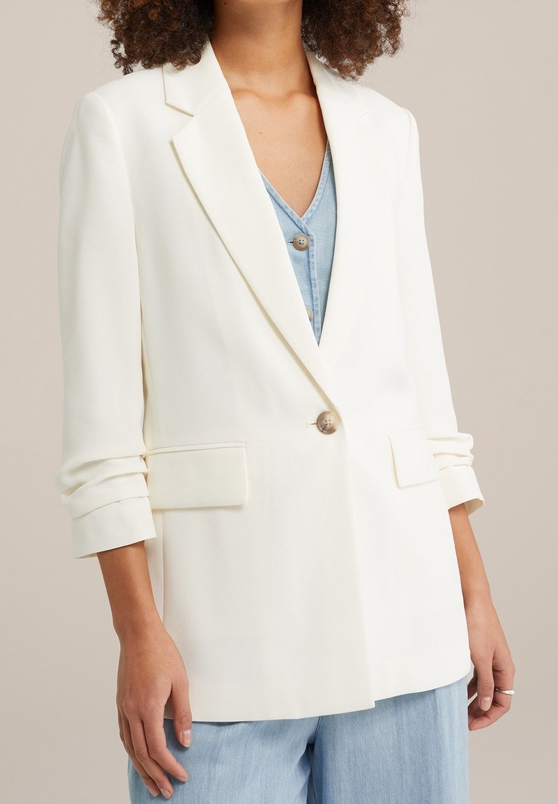 Biała marynarka o dopasowanym kroju, z klapami z wycięciem, pojedynczym guzikiem oraz podwiniętymi rękawami; gładka tekstura i dwie przednie kieszenie.