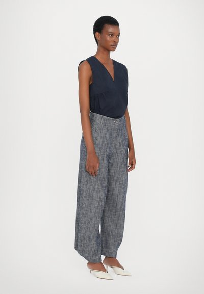 Top senza maniche blu navy con scollatura a V, abbinato a pantaloni ampi texture blu chiaro e mule bianche con punta affusolata. Design semplice e moderno.