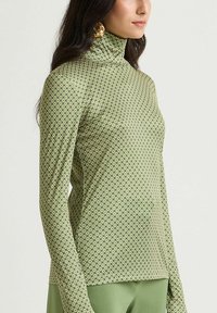 Maglione a collo alto verde con maniche lunghe, caratterizzato da una stampa geometrica e un design aderente, realizzato in un tessuto liscio.