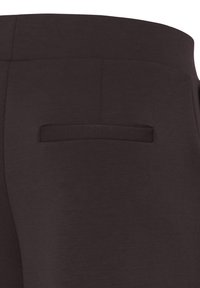 Détail de la poche arrière d’un pantalon marron foncé sur mesure avec une poche passepoilée et une couture à la taille.
