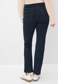 Donkerblauwe denim jeans met een slim fit en een middel hoge taille, voorzien van twee achterzakken en een rechte pijpdesign. Gecombineerd met witte sneakers.