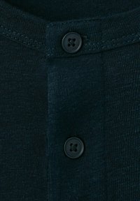 Detailný záber tmavomodrej pleteniny s dvoma čiernymi štvordierkovými gombíkmi usporiadanými vertikálne na rebrovanom plisé.