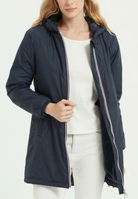 Veste rembourrée bleu marine avec une capuche, des poignets élastiques et une fermeture éclair à l'avant. Elle possède une doublure intérieure douce et un design mi-long.