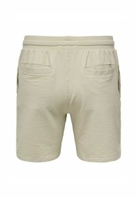Pantalones cortos beiges con una tela texturizada, cinturilla elástica y dos bolsillos traseros. Presentan un patrón sutil y un corte holgado.