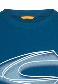 Niebieska bawełniana koszulka z okrągłym dekoltem, gładką fakturą oraz białym graficznym wzorem, który zakrzywia się na przodzie. Pomarańczowa metka wewnątrz kołnierzyka.