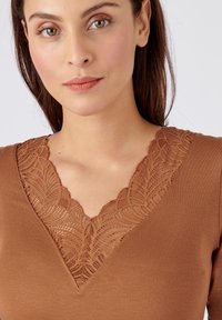 Bruine top met een V-hals en ingewikkelde kantdetails. Zachte stof en een getailleerd ontwerp benadrukken de halslijn.