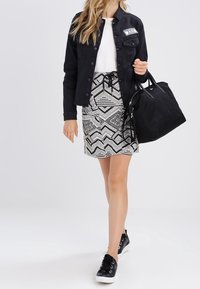 Giacca di jeans nera, top in rete bianco, gonna a righe nera e bianca con coulisse, sneakers nere, che porta una borsa a tracolla nera.