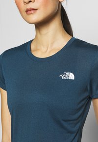 Mörkblå t-shirt med rund hals och korta ärmar. Har en liten vit logo på vänster bröst. Slät tygstruktur.