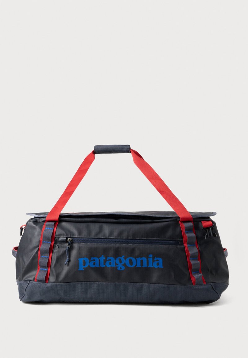 Črn najlon torba s rdečimi trakovi, modrim logotipom "patagonia", žepom na zadrgo, ravnim dnom, trpežno teksturo in stranskimi stisnimi trakovi.