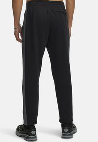 Black sweatpants with an elastic waistband, side stripes, and back pocket. Made of soft, smooth fabric, fitted at the ankle.