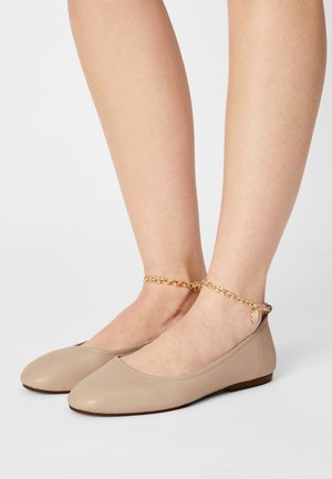 Ballerines en cuir beige avec un bout rond et une semelle plate. Présentent un détail de chaîne dorée à la cheville avec une petite plaque d'accent.