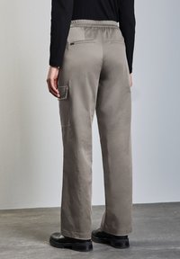 Ljus khaki avslappnade byxor med elastisk midja, bakfickor och en cargo-ficka på vänster sida. Slät textur och rak ben-design.