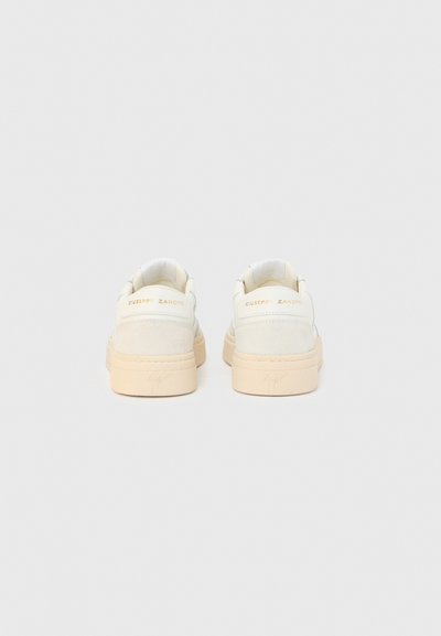 Valged mokkanahast tossud beežide kummist tallaga, mis on ülaosast sileda pinnaga, varustatud pehme kraega ja kannaosas reljeefse kaubamärgi nimega.