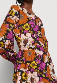 Blumenkleid mit lebhaften orangefarbenen, rosa und gelben Blumen auf schwarzem Hintergrund, langen Ärmeln und einem elastischen Taillenbund.