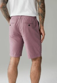 Lys lilla shorts med elastisk talje, to baglommer med knaplukninger og et struktureret stof.