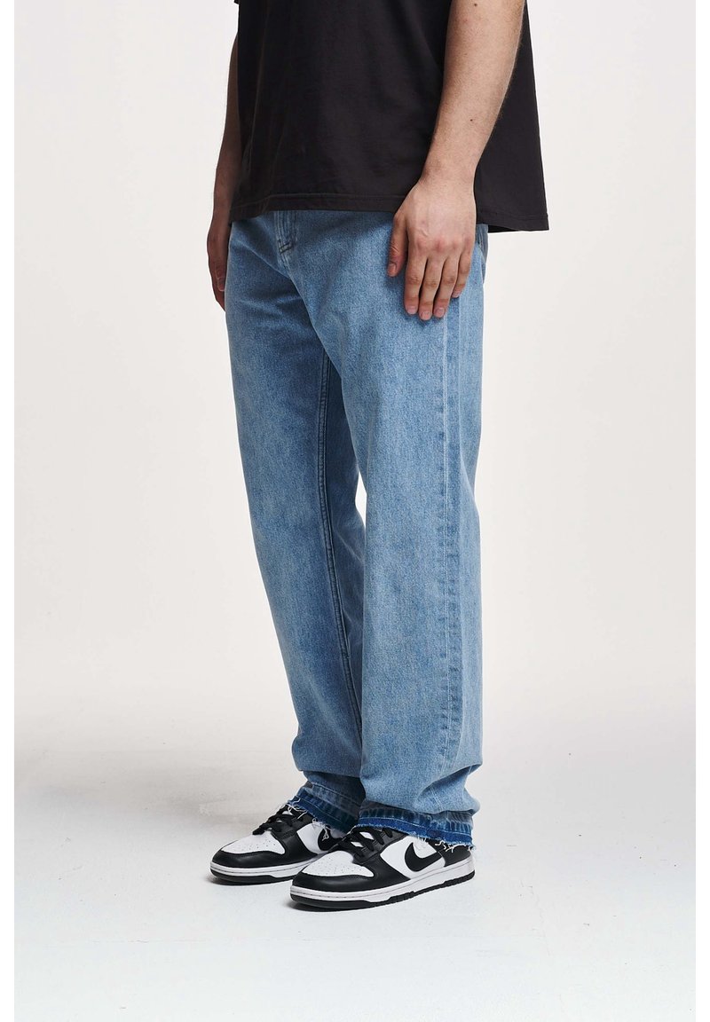 Vaqueros azules claros de corte recto, hechos de mezclilla, combinados con zapatillas negras y blancas con cordones y un logotipo de marca visible.