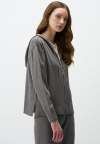 Sweat à capuche zippé gris avec une capuche, des manches longues, des fentes sur les côtés et un tissu texturé, associé à un bas assorti.