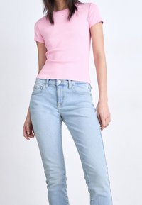 Rosa ribbad t-shirt med korta ärmar, i kombination med ljusblå tajta jeans. T-shirten har en liten logotyp på bröstet.