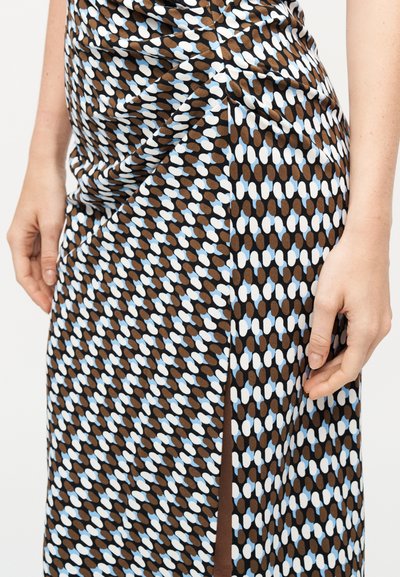 Κοντινό πλάνο ενός φόρεματος με μοτίβο από καφέ, λευκούς και γαλάζιους οβάλ σχήματα, με πλαϊνή σχισμή και μερικώς ορατά χέρια.