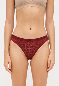Sarkans mežģīņu bikini apakšveļa ar melnu Calvin Klein logotipu jostasvietā. Iespējots pusskaidrs raksts un augstas kājas dizains.
