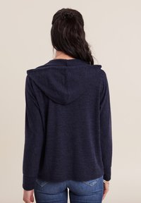 Felpa navy blu in tessuto morbido e testurizzato, con una vestibilità rilassata, maniche lunghe e cappuccio con cordino. Dettagli delle cuciture visibili sul retro.