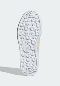 White rubber sneaker sole with circular and patterned treads. Accented with light beige textile along the sides. Adidas logo at center.