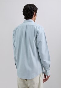 Lichtblauw gestreept overhemd met knopen, gezien van achteren, met lange mouwen en een afgeronde zoom voorzien van een kleine kraag, gemaakt van zachte stof.